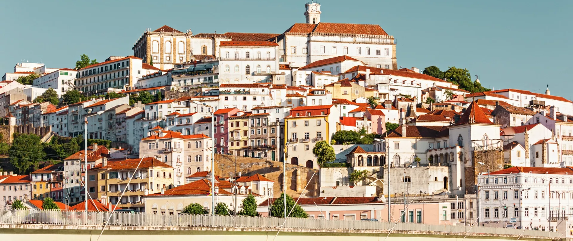 Scenic view of the University of Coimbra hilltop, a UNESCO World Heritage Site, with historic buildings and traditional houses at sunset.
