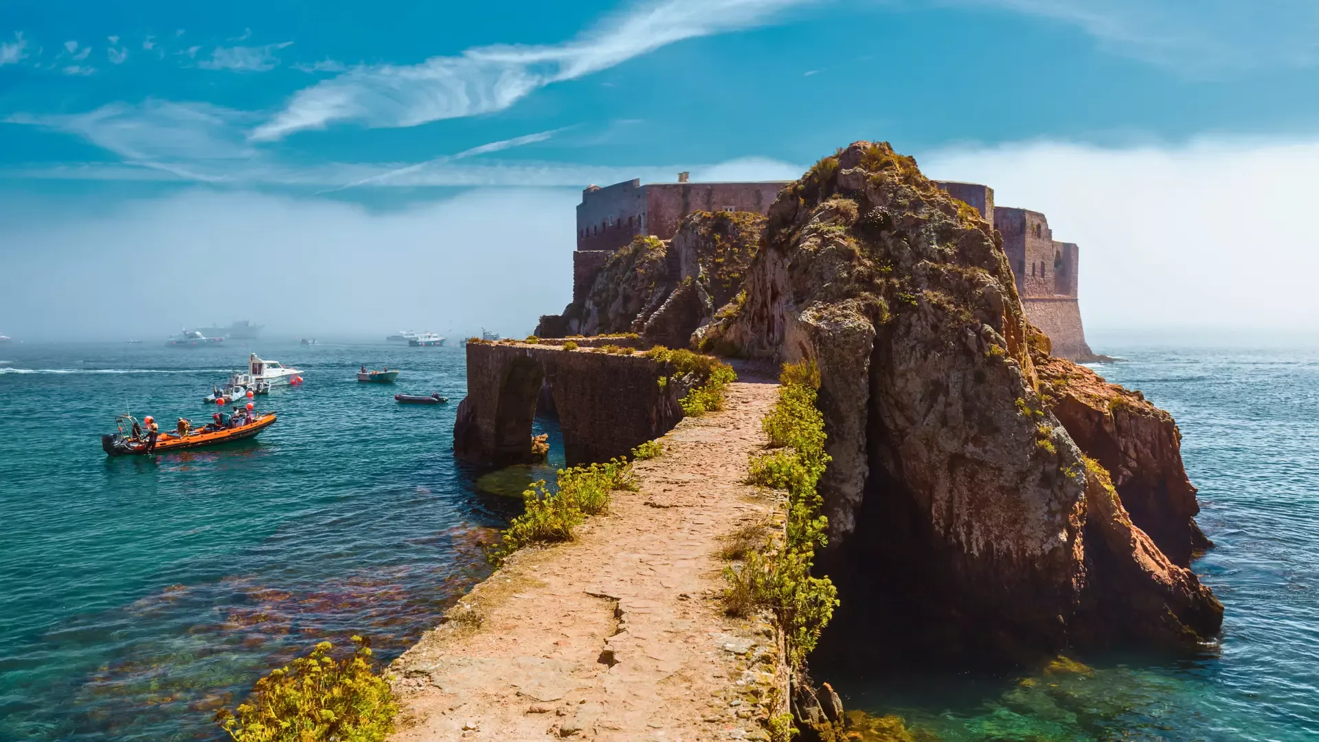 Stone path leading to the Fortress of São João Baptista on Berlenga Island, surrounded by turquoise Atlantic waters and boats.