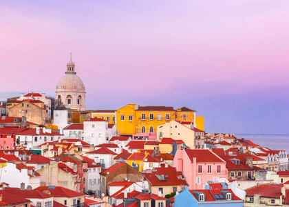 Colorful view of the Alfama district in Lisbon, Portugal, at sunset with the dome of the National Pantheon in the background.