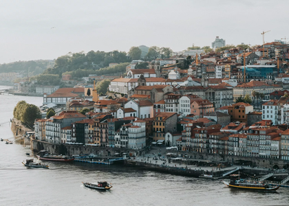 Panoramic view of Porto’s Ribeira with traditional rabelo boats on the Douro River and Arrábida Bridge in the distance.