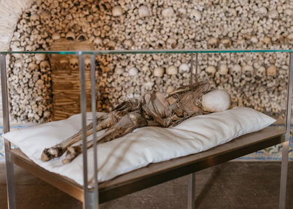 Interior view of the Chapel of Bones in Alcácer do Sal, Portugal, featuring a mummified body on display and walls covered with human skulls and bones.