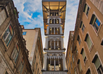 View from below of the Santa Justa Lift in Lisbon, Portugal, with its neo-Gothic iron structure illuminated against the evening sky.
