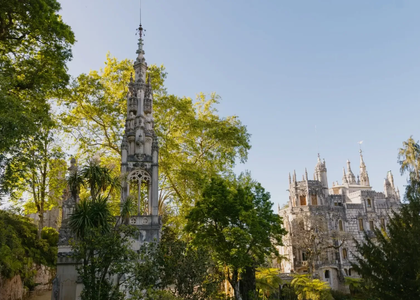 View of the Gothic tower and main palace of Quinta da Regaleira in Sintra, Portugal, surrounded by lush greenery under a clear blue sky.