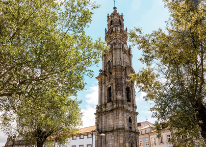 Clérigos Tower in Porto, Portugal, surrounded by green trees under a blue sky.