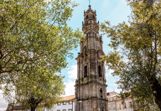 Clérigos Tower in Porto seen through lush green trees on a sunny day in the historic city center.