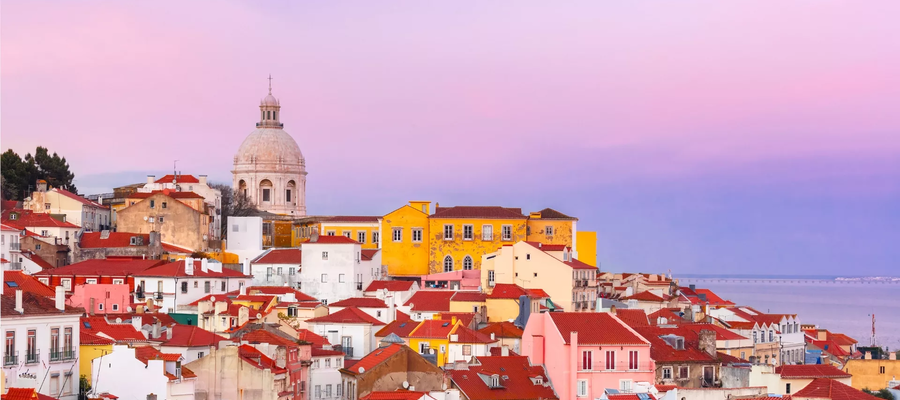 Colorful view of the Alfama district in Lisbon, Portugal, at sunset with the dome of the National Pantheon in the background.
