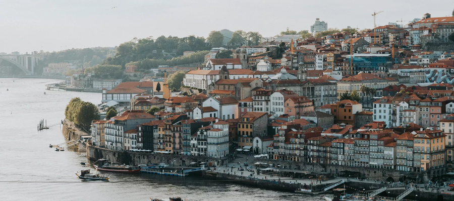 Panoramic view of Porto’s Ribeira with traditional rabelo boats on the Douro River and Arrábida Bridge in the distance.
