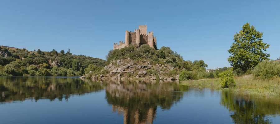 View of Almourol Castle on a small island in the Tagus River, surrounded by nature and reflected in the calm water