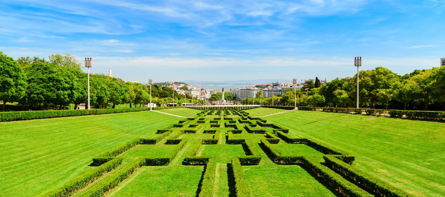 View of Eduardo VII Park in Lisbon, Portugal, with its symmetrical hedges, green lawns, and cityscape in the background.