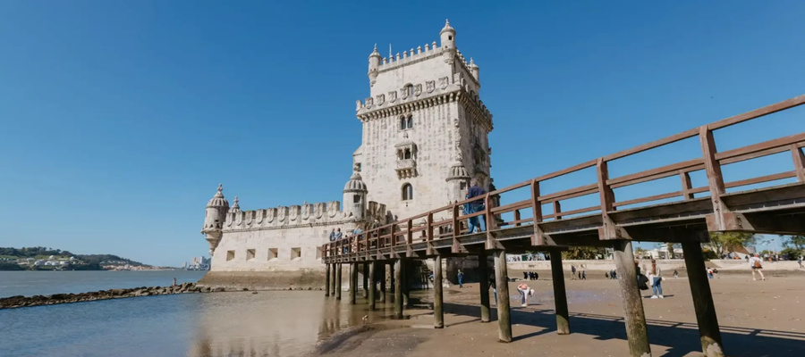 Belem Tower in Lisbon, Portugal, with wooden walkway and people exploring the beach at low tide.