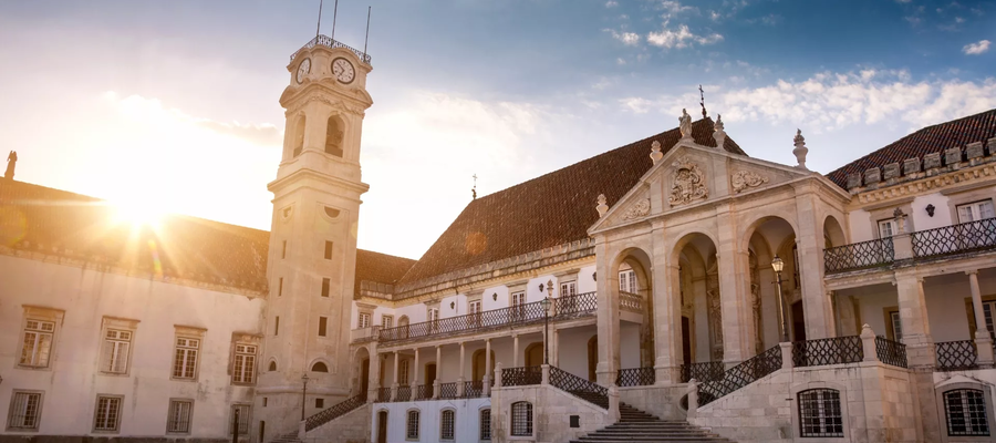 Main façade of the University of Coimbra with the iconic clock tower glowing in the golden sunset light.
