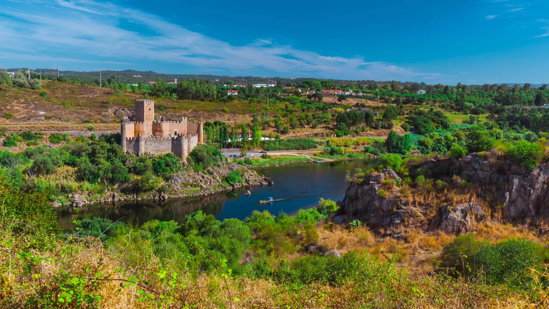 Aerial view of the medieval Almourol Castle on a small island in the Tagus River, surrounded by lush green hills and calm waters.