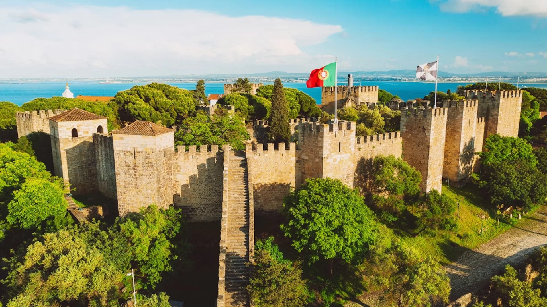 Aerial view of São Jorge Castle in Lisbon, Portugal, with medieval walls, flags, and view over the Tagus River.