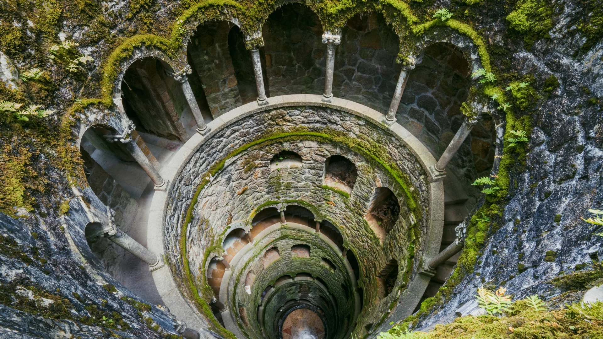 Initiation Well of Quinta da Regaleira in Sintra, Portugal, with spiral staircase and moss-covered walls.