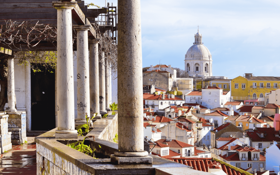 View from the Santa Luzia viewpoint in Lisbon, Portugal, with traditional tiled columns and a panoramic scene over Alfama's rooftops and the National Pantheon dome.