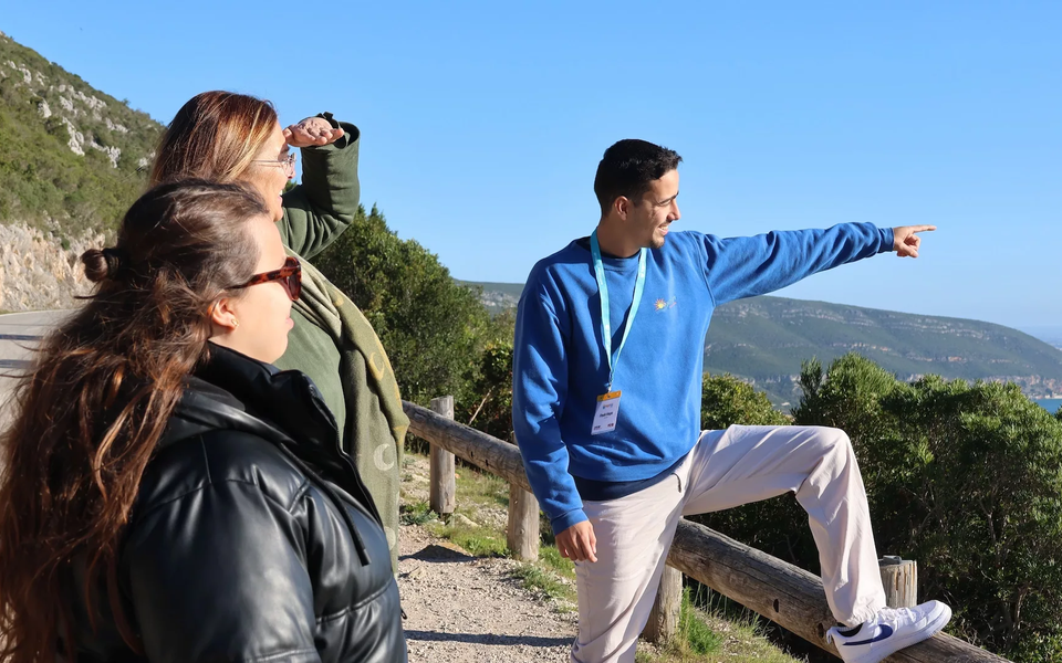 Tour guide pointing towards Tróia while explaining the panoramic landscape from the Arrábida viewpoint.