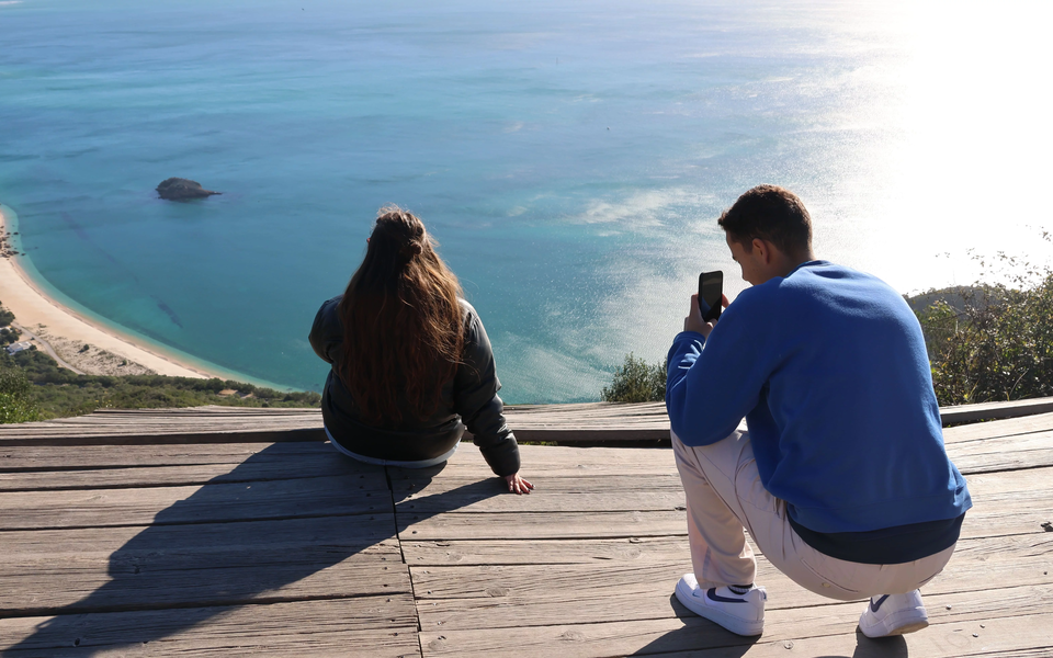 Couple enjoying the panoramic view over Figueirinha Beach from a viewpoint in the Arrábida Natural Park, Portugal.
