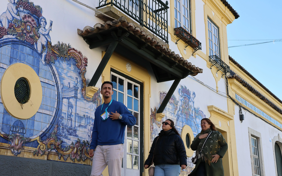 Visitors walking past a tiled façade with blue and white azulejos at the Palácio Caldeira in São Simão, Portugal.