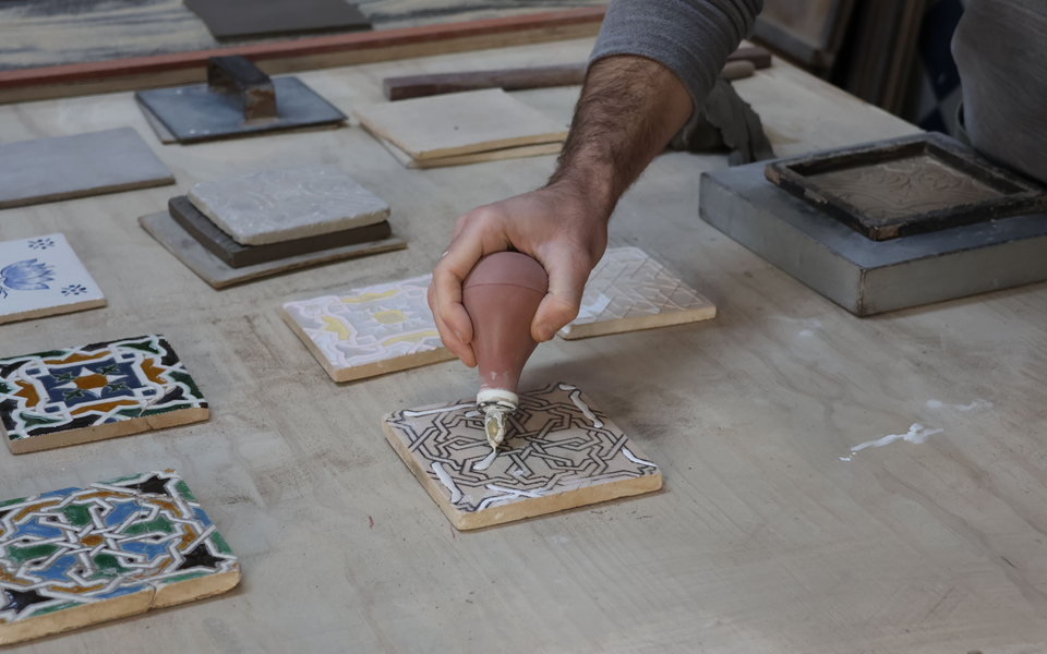 Close-up of a craftsman decorating a traditional Portuguese tile by hand using a piping tool.