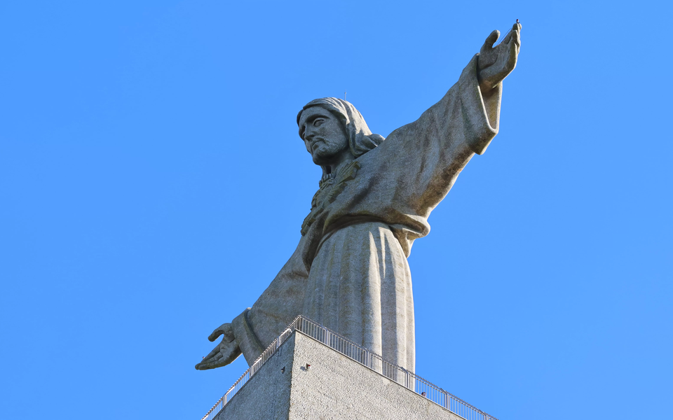 Low-angle view of the Christ the King monument in Almada, Portugal, against a clear blue sky.