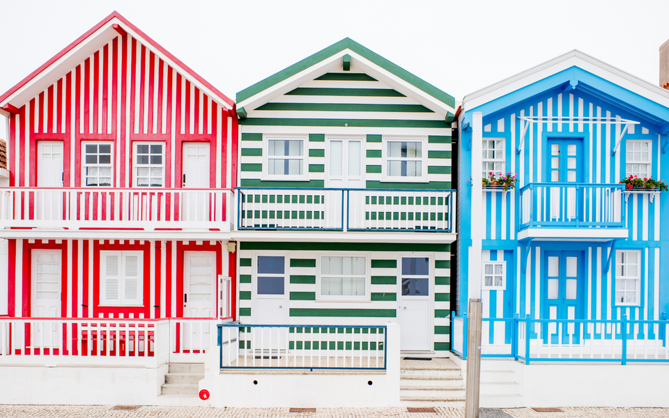 Colorful striped houses in Costa Nova, Aveiro, Portugal. Traditional wooden homes painted in vibrant red, green, and blue stripes.