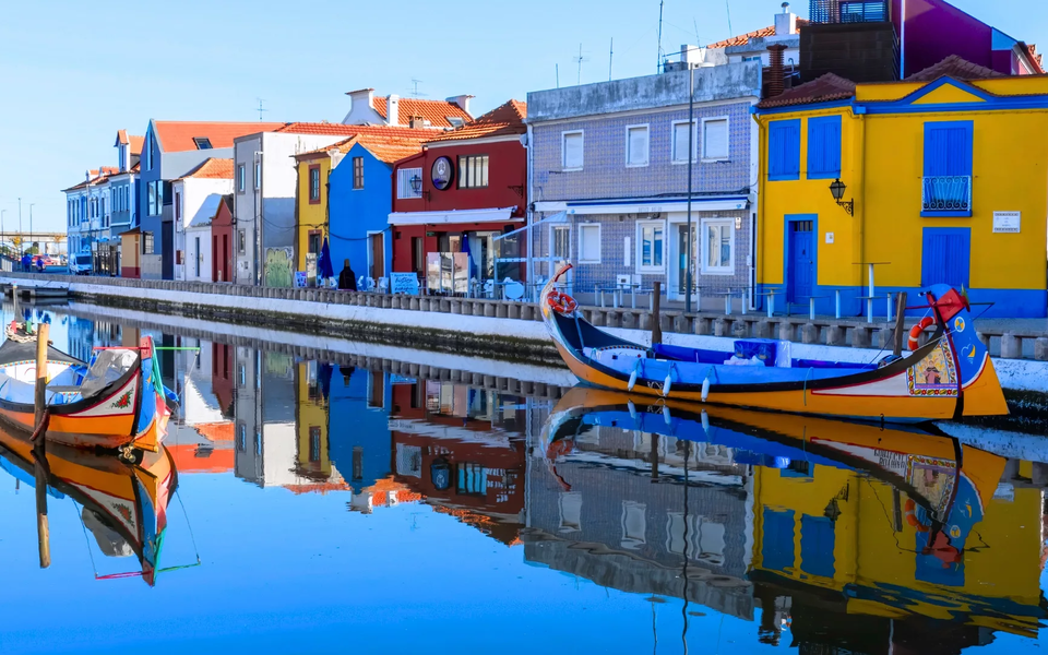 Moliceiro boats on the canal in Aveiro, Portugal, with colorful houses reflecting in the water.