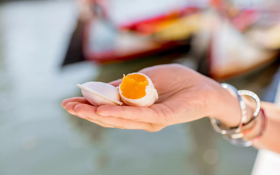 Traditional Portuguese sweet "Ovos Moles" held in a hand, with Aveiro's colorful moliceiros blurred in the background.