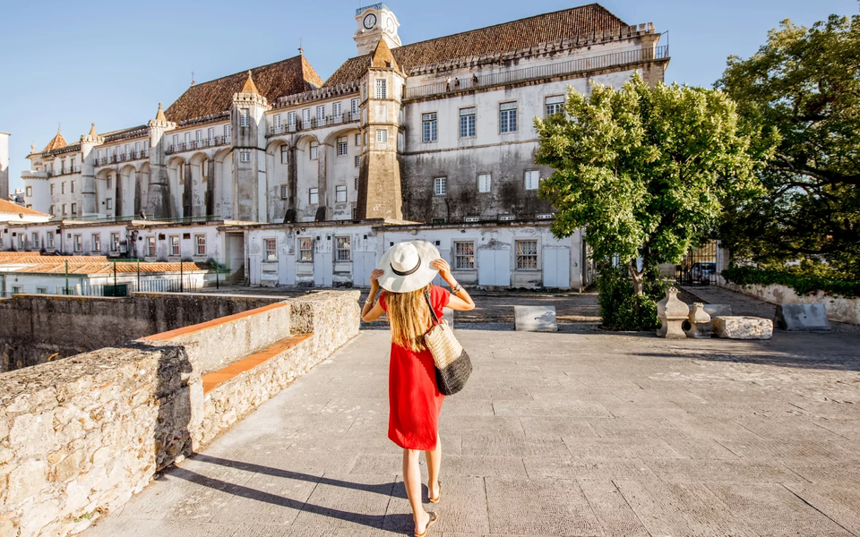 Female tourist in a red dress and sunhat walking towards the University of Coimbra in Portugal, a UNESCO World Heritage Site.