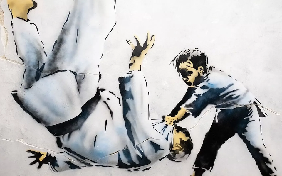 Stencil artwork of a child throwing an adult in a judo move, created by Banksy and displayed on a cracked wall, symbolizing themes of power and role reversal.