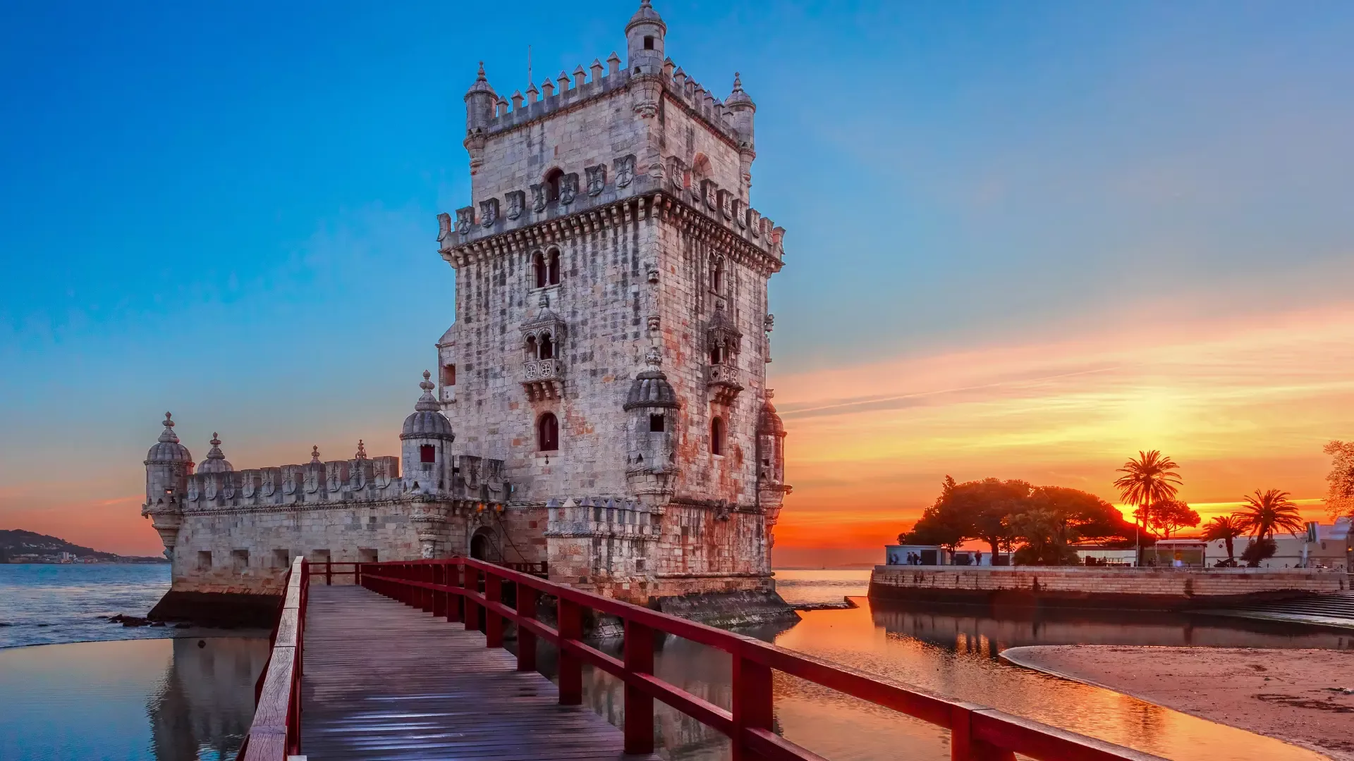 Belem Tower in Lisbon at sunset with warm orange skies reflecting on the Tagus River, showcasing one of Portugal’s most iconic landmarks.