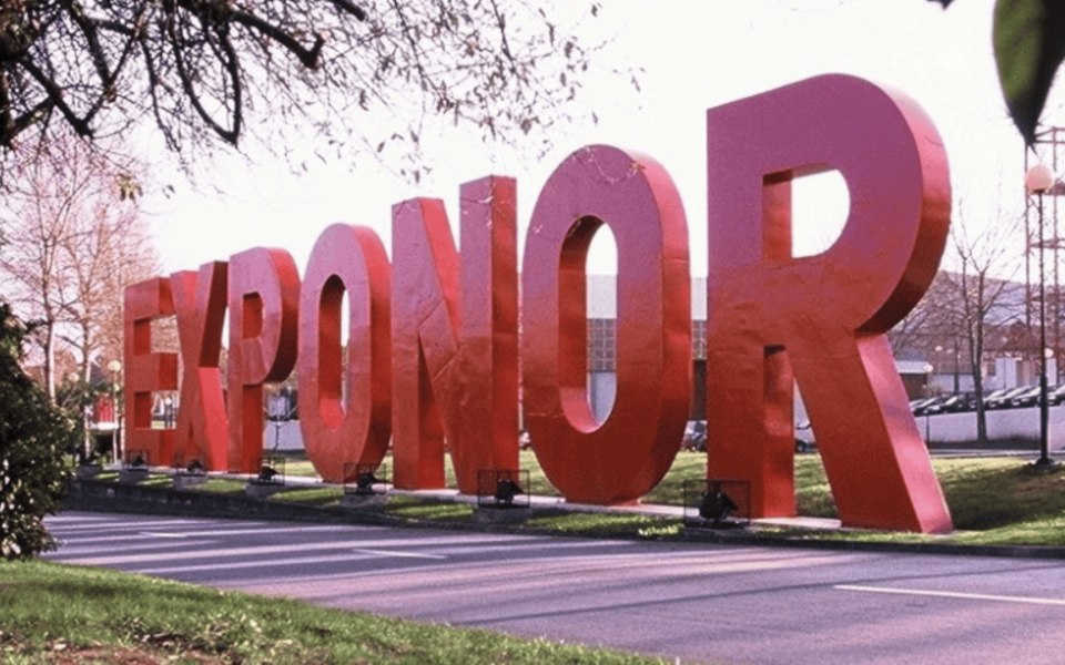 Large red letters spelling "Exponor" at the main entrance of the Exponor trade fair and congress center in Porto, Portugal. The image showcases the landmark signage along a tree-lined road near the exhibition venue.