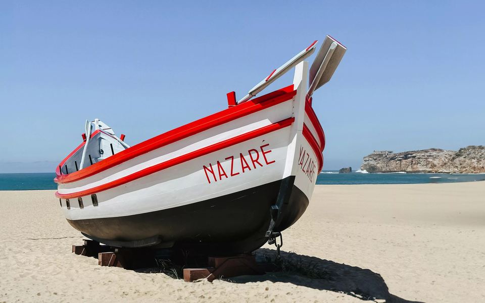 Wooden fishing boat painted with "Nazaré" on the sandy beach by the ocean