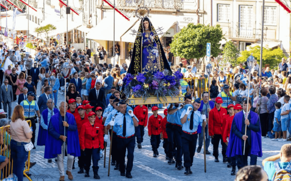 Religious procession of Our Lady of Sorrows during Feiras Novas festival in Ponte de Lima, Portugal. Uniformed participants carry a richly decorated statue through the cobbled streets, surrounded by a large crowd of spectators during a sunny afternoon.