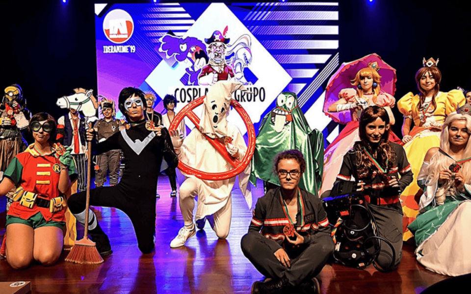 Group of cosplayers posing on stage at Iberanime 2025 in Portugal, during the cosplay contest. Participants wear elaborate costumes from anime, video games, and pop culture franchises, set against a vibrant backdrop featuring the event’s branding.