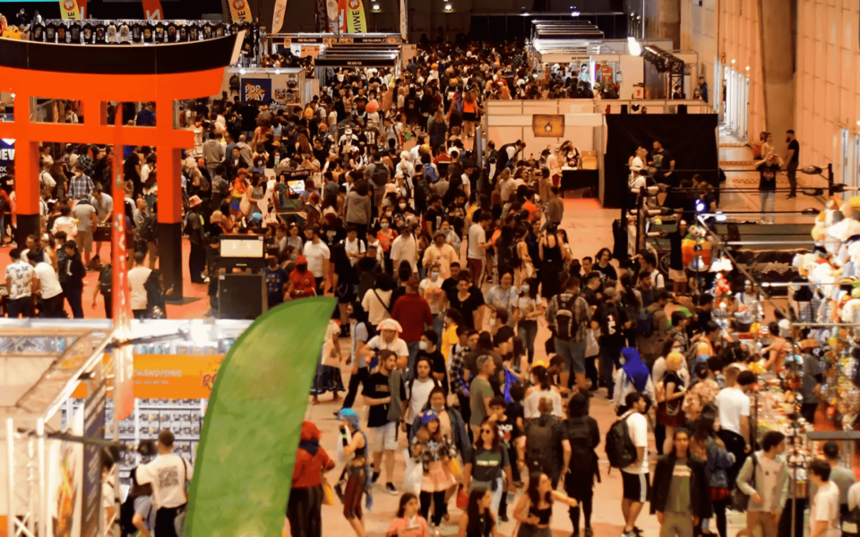 Crowded overview of Iberanime 2025, Portugal’s largest Japanese pop culture event held at Exponor in Porto. The image shows dozens of booths, visitors in cosplay, and a prominent red torii gate, capturing the vibrant atmosphere of the convention.