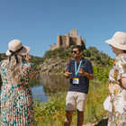 Tour guide explaining the history of Almourol Castle in Tomar, Portugal, with visitors by the river.