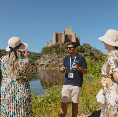 Tour guide explaining the history of Almourol Castle in Tomar, Portugal, with visitors by the river.