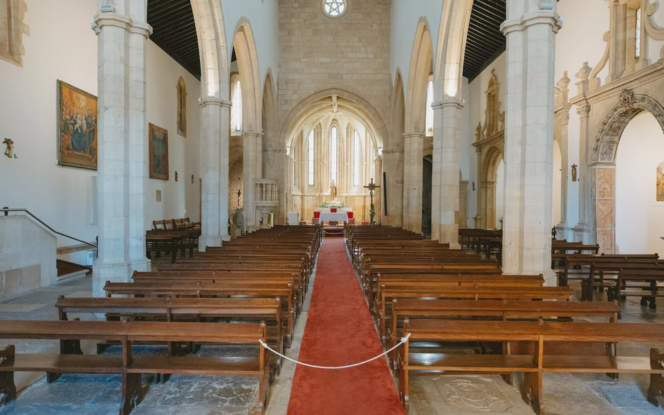 Interior view of the Church of Santa Maria do Olival in Tomar, Portugal, with Gothic arches and wooden benches.