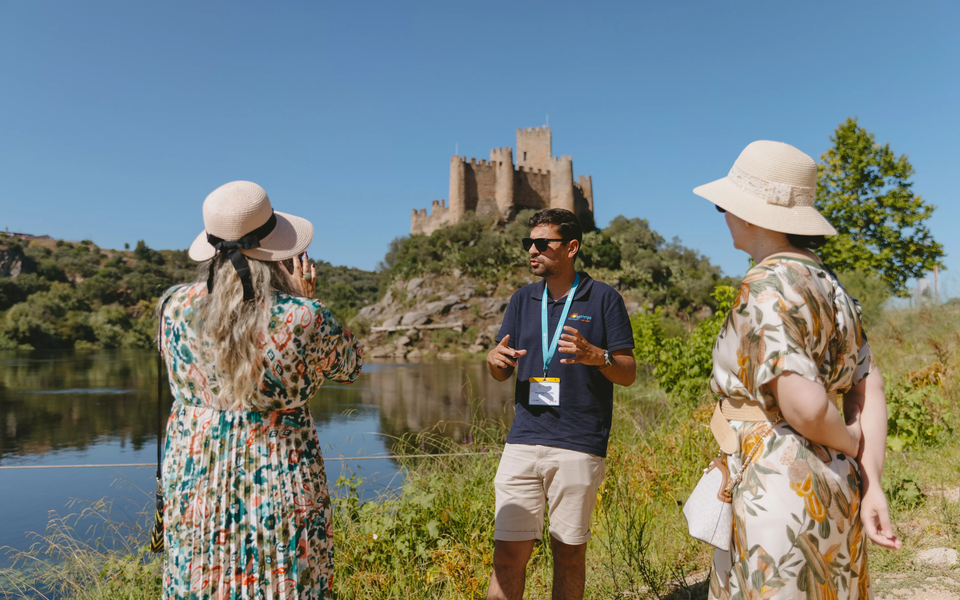Tour guide explaining the history of Almourol Castle in Tomar, Portugal, with visitors by the river.