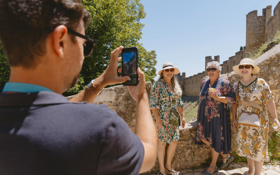 Tour guide taking a picture of three smiling tourists by the medieval castle walls in Tomar, Portugal.