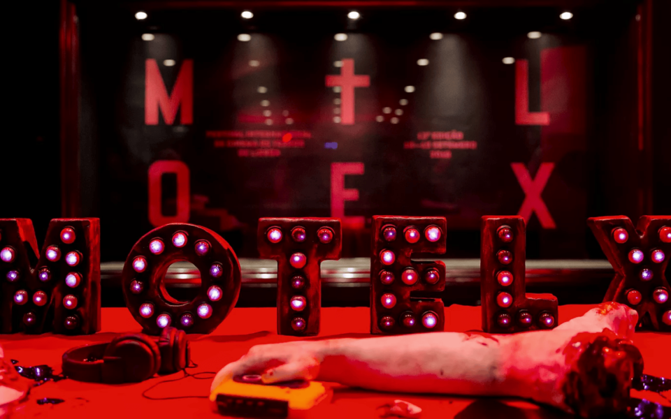 Horror-themed display at MOTELX with glowing red "MOTELX" letters, fake blood-covered props, severed limb decoration, and eerie lighting. The background includes reflective surfaces and thematic typography, enhancing the immersive cinematic horror atmosphere.