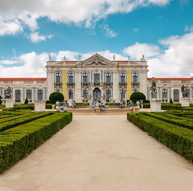 Baroque façade of the National Palace of Queluz with manicured gardens and statues under a blue sky with clouds.