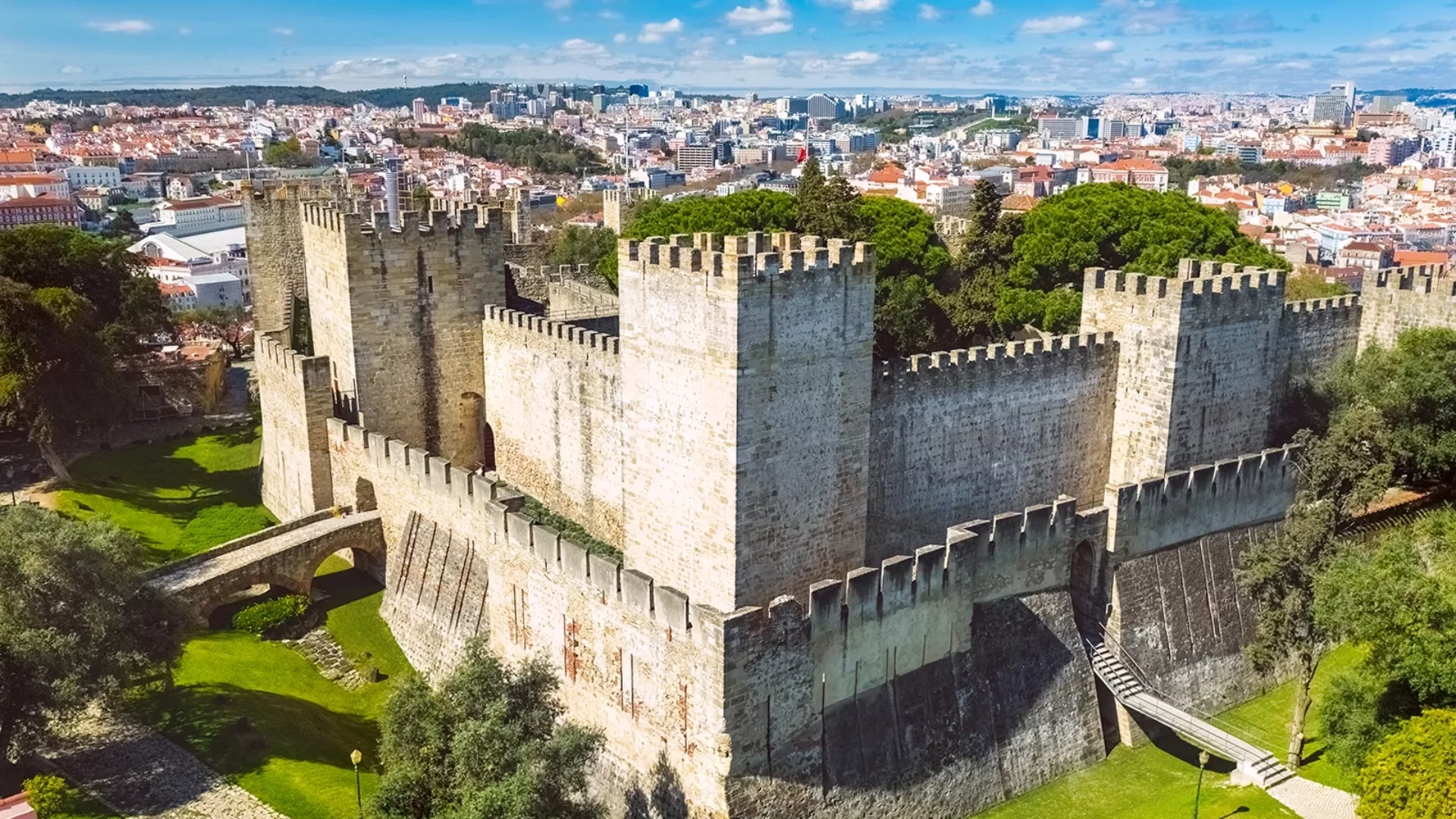 View of the medieval walls and towers of São Jorge Castle in Lisbon, Portugal, with flags flying on top.