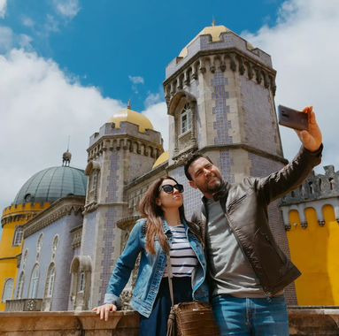 A happy couple takes a selfie in front of the stunning Pena Palace in Sintra, Portugal, capturing a beautiful moment together.