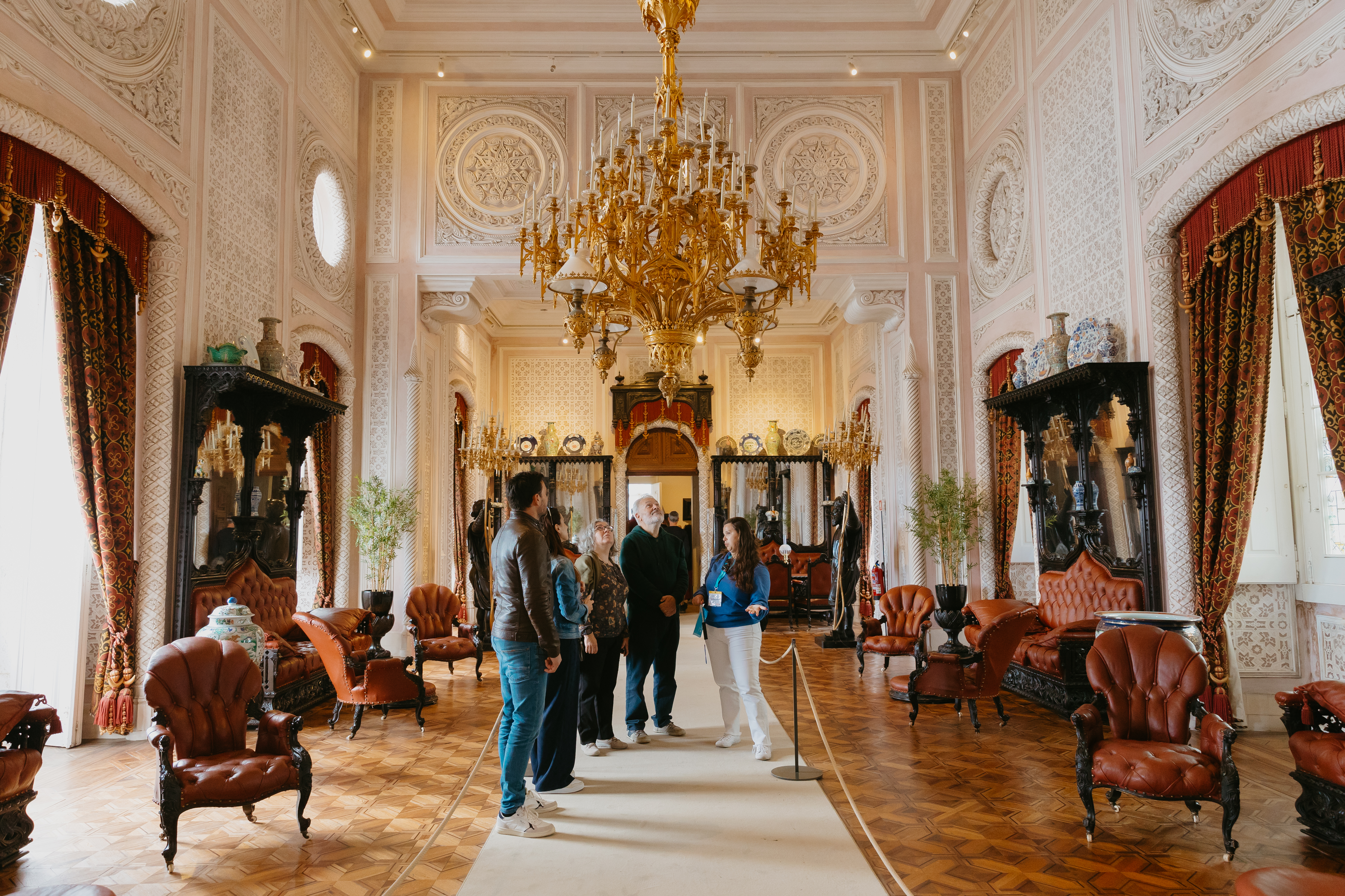Guests explore the majestic grand hall of Pena Palace in Sintra, admiring a beautiful chandelier during a guided tour.