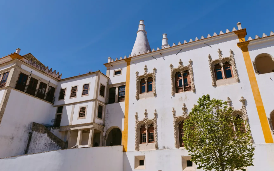 Side view of the National Palace of Sintra with Manueline windows and iconic conical chimneys under a clear blue sky.
