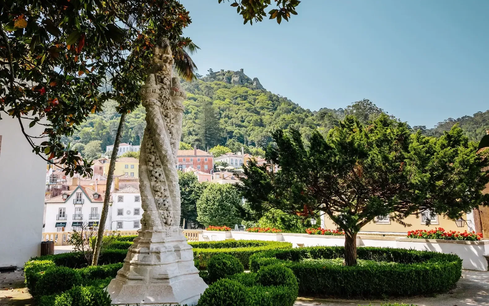 Manueline-style stone pillory in the gardens of the National Palace of Sintra with scenic views of the town and surrounding forested hills.