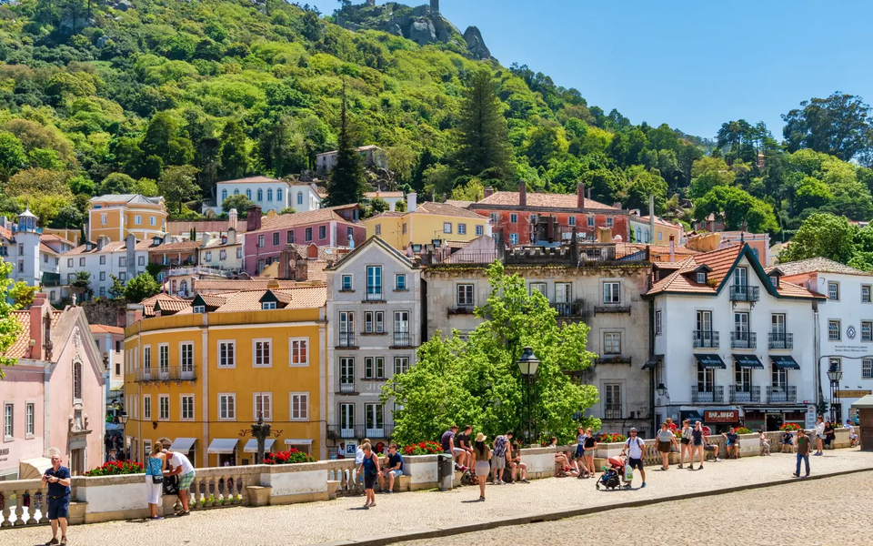 Colorful traditional buildings in the historic center of Sintra with lush green hills in the background.