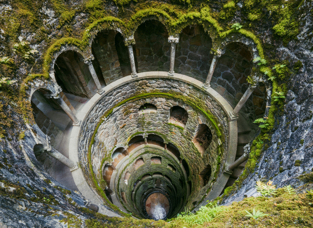 Inside the initiation pit at Quinta da Regaleira, a stone tunnel adorned with lush moss creates a mystical and serene atmosphere.