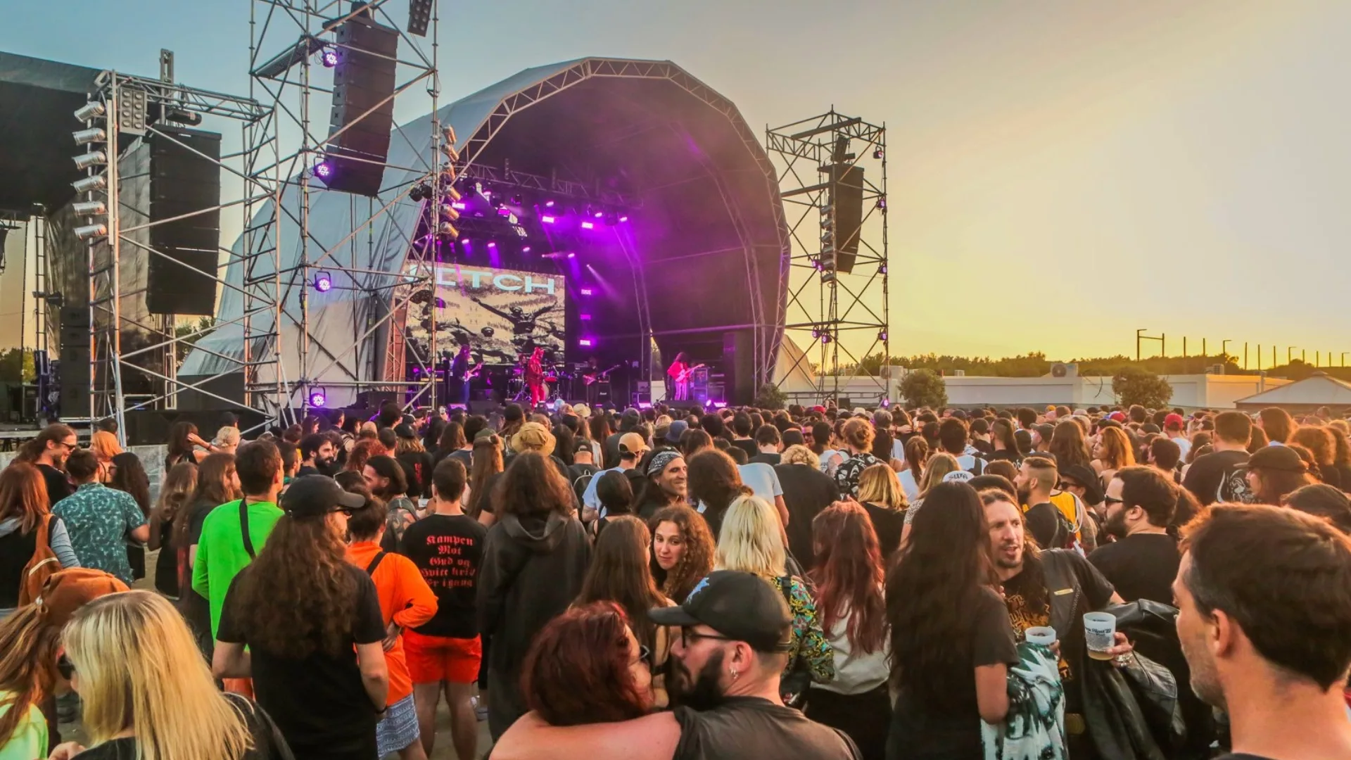 Crowd enjoying a heavy metal festival in Portugal at sunset with purple stage lights and live band performance.